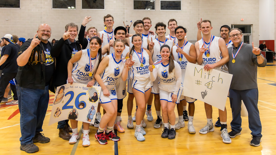 Dr. Priest stands for a group photo with Touro Nevada faculty and the university basketball team on the court. The team wears metals and holds up their index figure to signify their number one win.