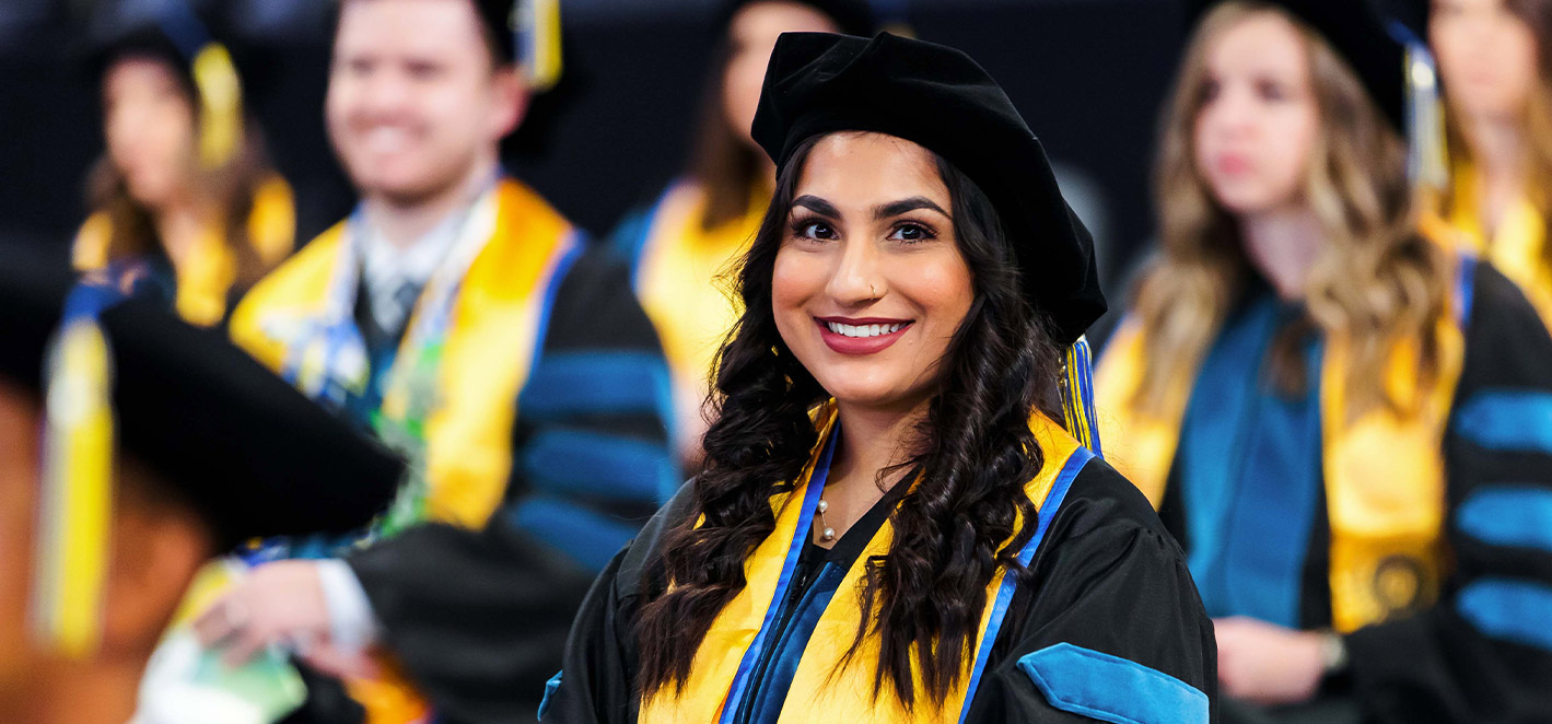 Graduate student in cap and gown smiles at the camera during the ceremony.