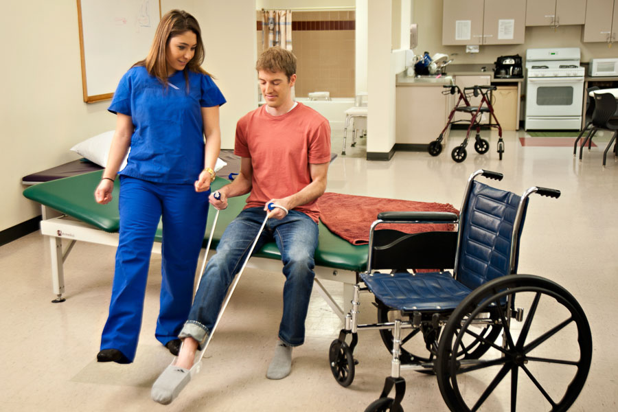 A physician shows a patient sitting on an exam table how to use a resistance band