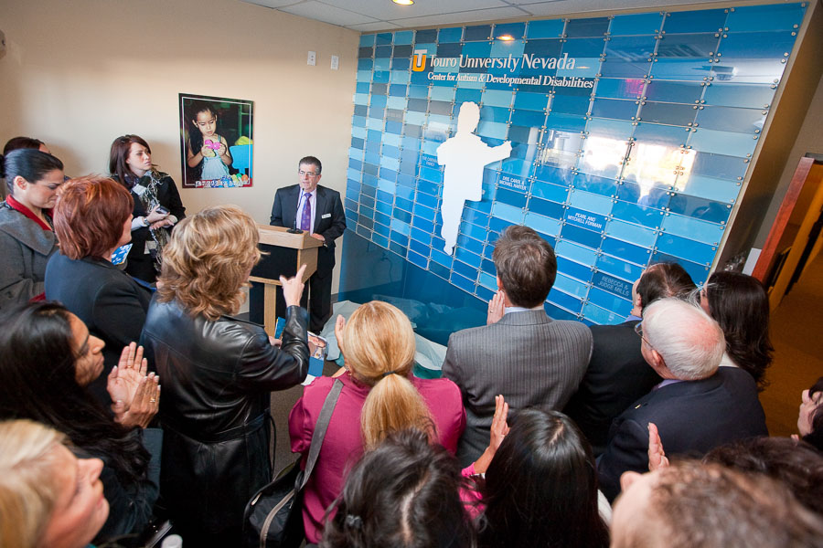 A large group of people gather for the opening ceremony in front of the Center for Autism sign