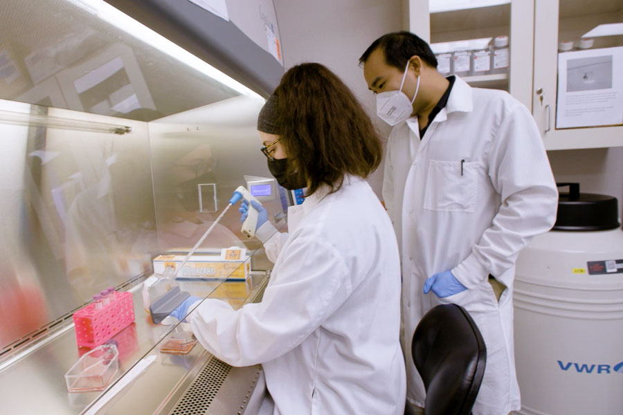 A student and faculty member in protective gear work in the research lab