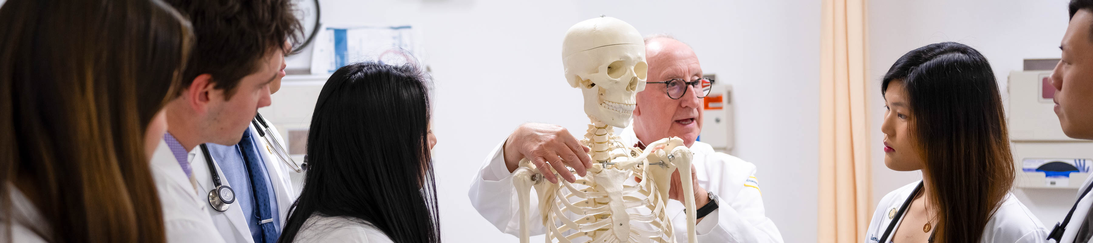 Dr. Gilliar teaches a group of Osteopathic Medicine students gathered around a skeleton model in a classroom.