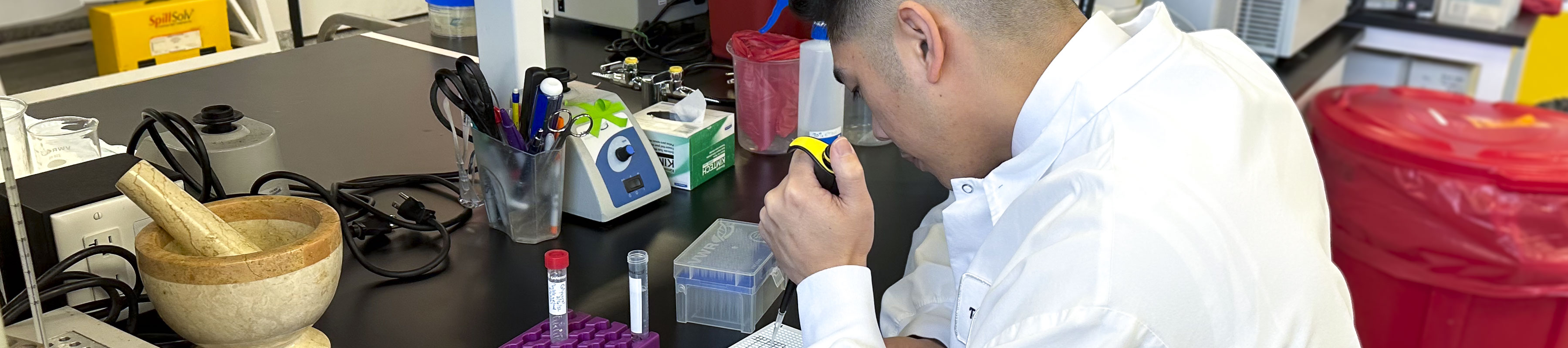 A research student wearing a white coat performs a test in a laboratory.