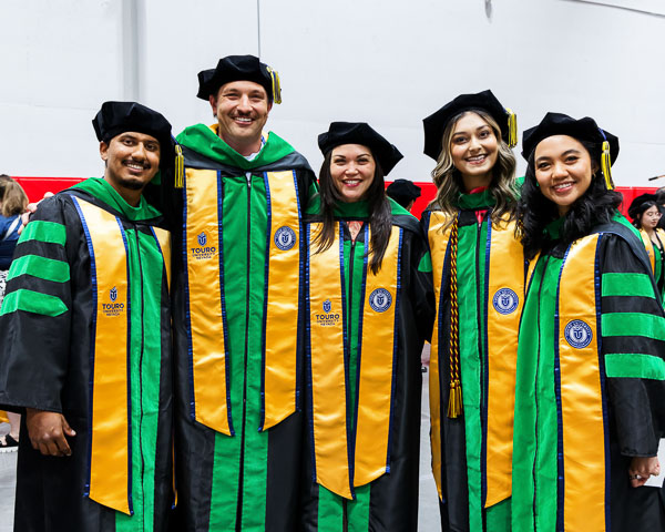 Five DO students in commencement regalia posing together at the ceremony