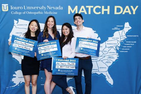 Four students in front of a United States map holding their Match Day signs