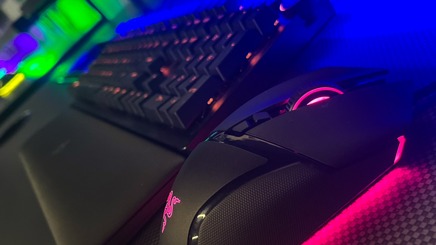 An led lit computer mouse and keyboard on a long gaming desk.