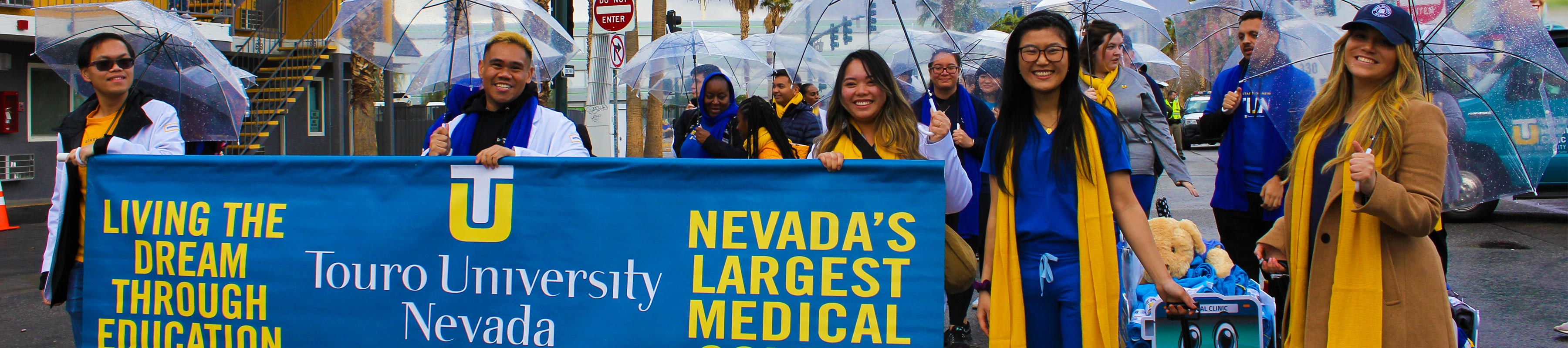 Students marching in a parade with a Touro Nevada banner.