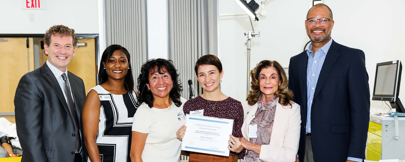 A future Touro student is presented with her certificate of scholarship while the group poses for photo in the Michael Tang Regional Center for Clinical Simulation.