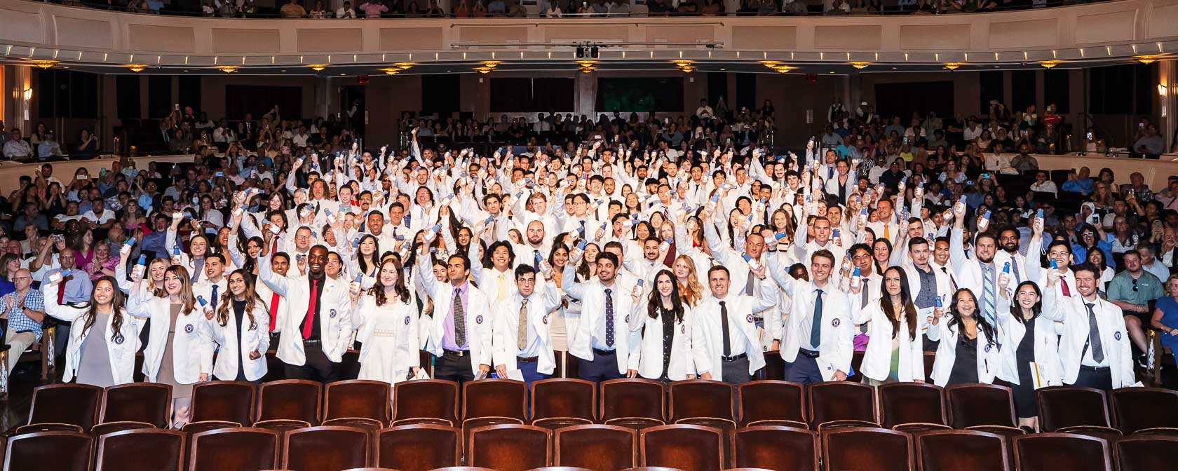 College of Osteopathic Medicine students in white coats hold up their personal portable ultrasound devices during the ceremony in the Smith Center theater.