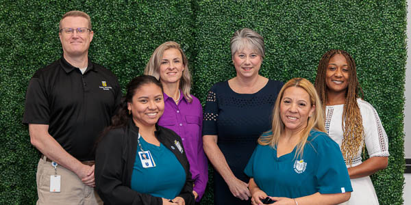 Six 10-year employees gather for a group photo in front of a greenery wall.