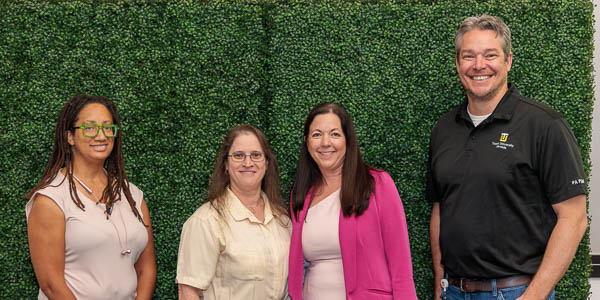 Four 15-year employees gather for a group photo in front of a greenery wall.