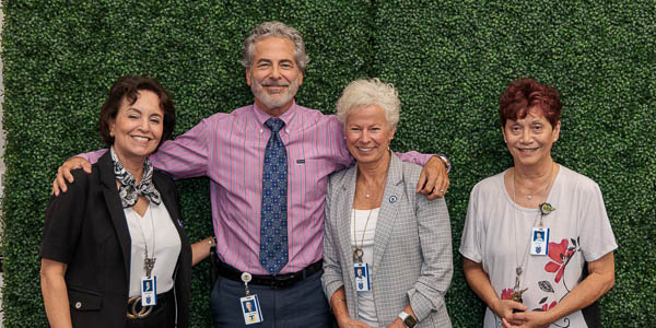 Four 20-year employees gather for a group photo in front of a greenery wall.