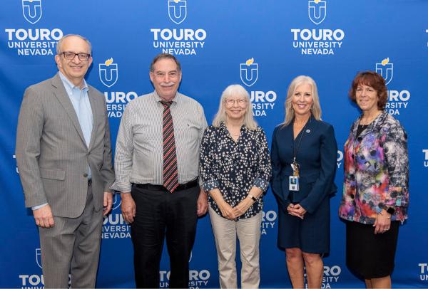University leadership takes a group photo with the fifteen-year faculty and staff during the 2025 employee recognition event in front of the Touro University Nevada logo.