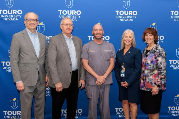 University leadership takes a group photo with the twenty-year faculty and staff during the 2025 employee recognition event in front of the Touro University Nevada logo.