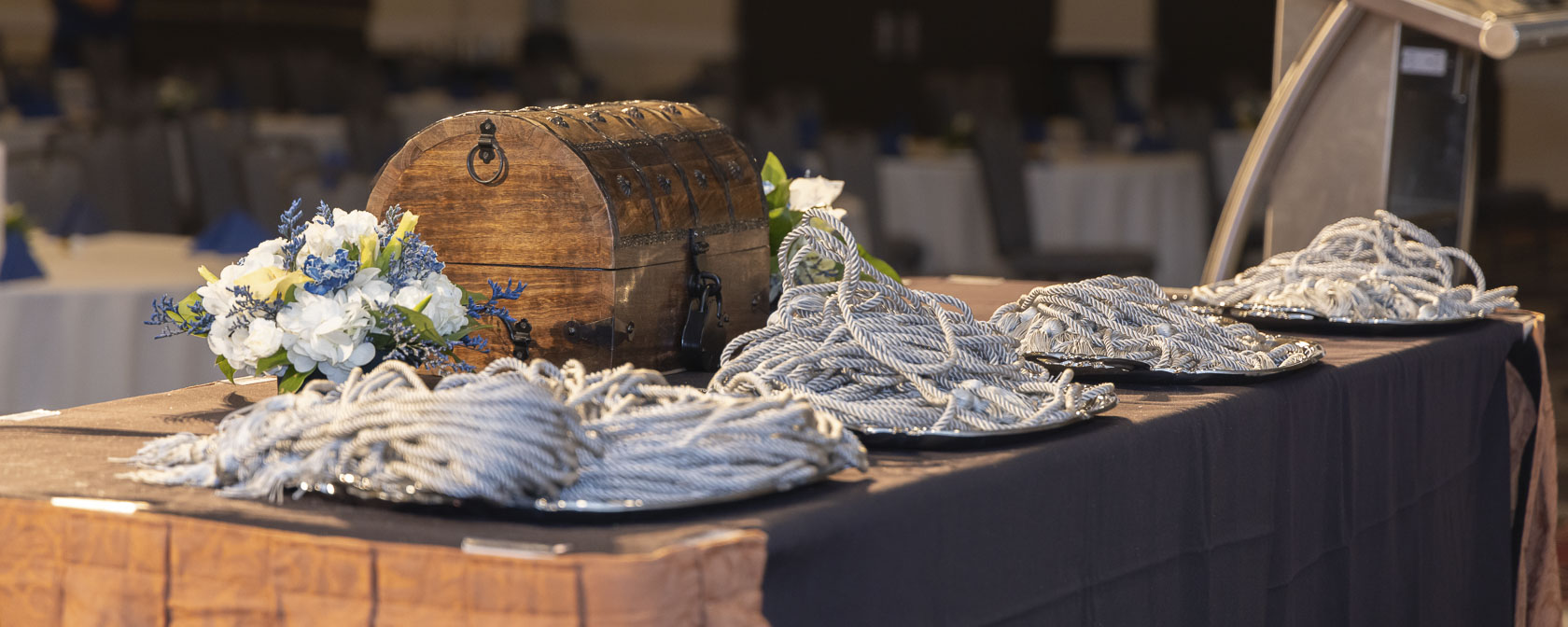 A chest holding the students eagerly awaited Match Day letters sits on a table, surrounded by trays of graduation cords and vibrant flowers celebrating the occasion.