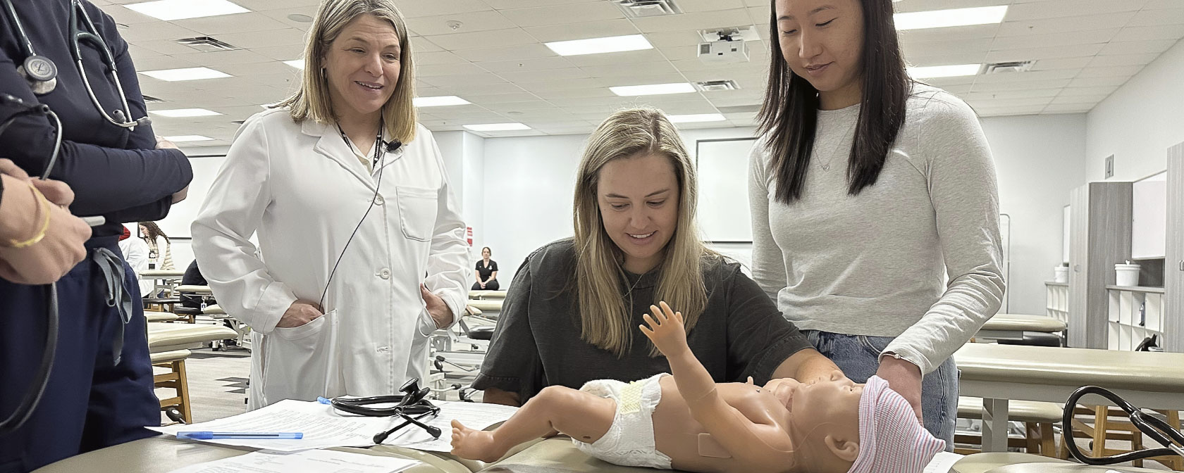 Two students examine a newborn simulation manikin during a pediatric simulation lab led by faculty.