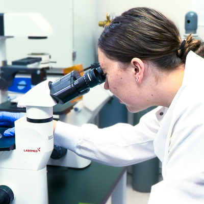 A woman in a white lab coat looking into a microscope.