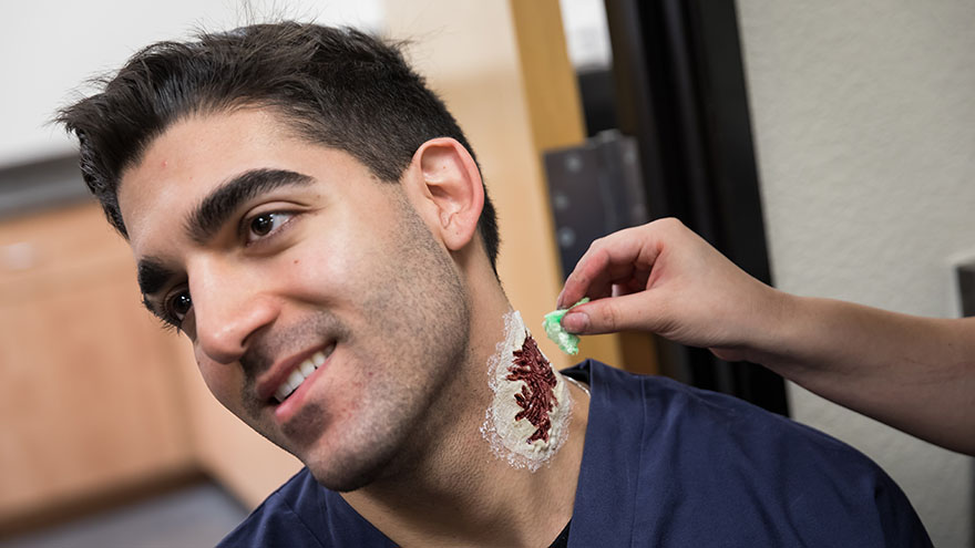 A makeup artist applies moulage on a student.  